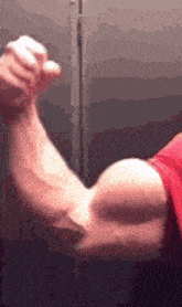 a man is flexing his muscles in front of a mirror while wearing a red shirt .