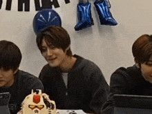 a group of young men are sitting at a table with a cake on it .