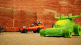 a green toy car with horns is next to a red toy car in the desert