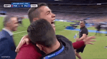 a man wearing a france lanyard hugs another man on a soccer field