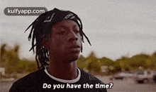 a man with dreadlocks is standing in a parking lot and asking do you have the time ?