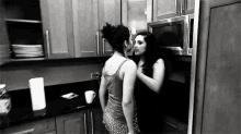 a couple of women are kissing in a kitchen .