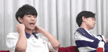 two young men are sitting on a couch one is laughing and the other is sleeping .