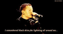 a man singing into a microphone with the words " i remembered black skies the lightning all around me " below him