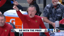 a man in a red shirt is pointing at a screen that says " go with the pros "