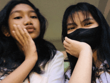 a girl wearing a black mask covering her mouth stands next to another girl
