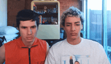 a man in an orange vest and a man in a white t-shirt are looking at each other