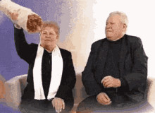 a man and a woman are sitting on a couch and the woman is holding a large burrito over her head