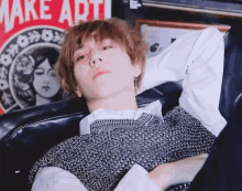 a young man is laying on a couch with a make art sign in the background