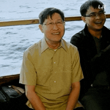 a man wearing glasses sits next to another man with the letters lje on the bottom right corner