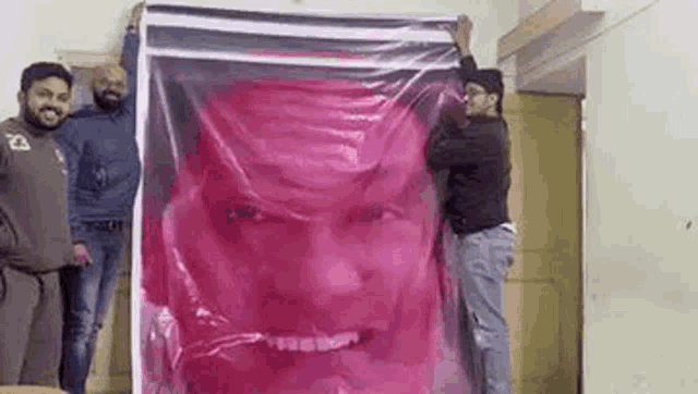a group of men are holding a large pink poster with a picture of a man 's face on it .
