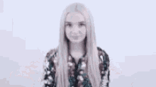 a woman with blonde hair is wearing a floral shirt and smiling with her eyes closed .