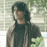 a man with long hair wearing a black shirt and brown jacket