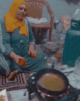 a woman in a yellow head scarf sits on the floor cooking food