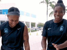 two women wearing nike shirts with ny on them are standing next to each other