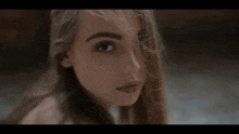 a woman with long hair is looking at the camera with her hair blowing in the wind .