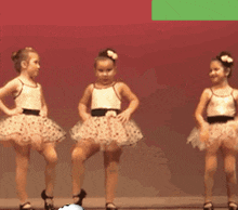 three little girls are dancing on a stage and one has a flower in her hair