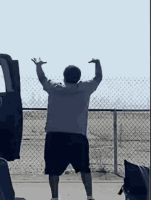 a man is standing with his arms in the air in front of a fence .