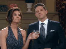 a man in a suit is holding a glass of whiskey next to a woman in a dress