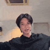 a young man in a black hoodie is standing in a room with a ceiling fan .