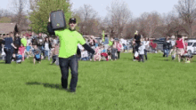 a man in a neon green shirt is holding a briefcase in a field with a crowd behind him .