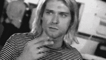 kurt cobain is wearing a striped shirt and smoking a cigarette in a black and white photo .