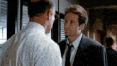 a man in a suit talks to another man in a white shirt