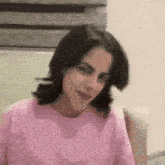 a woman in a pink sweater is sitting on a couch and making a funny face .