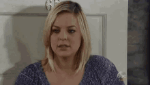 a woman in a purple shirt is standing in front of a door and making a funny face .
