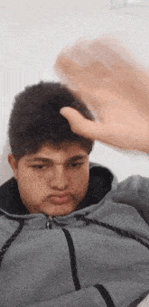 a young man in a grey hoodie is making a funny face while holding his hand to his head .