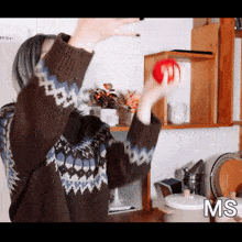 a woman in a sweater throws a red ball in the air with the letters ms visible in the corner