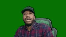 a man wearing a plaid shirt and a hat is sitting in front of a green background with the letter f visible