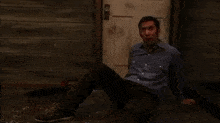 a man in a blue shirt is sitting on the floor in front of a door in a dark room .
