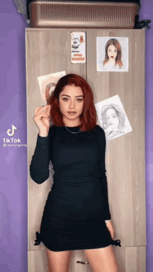 a woman in a black dress is standing in front of a purple wall with drawings of women on it ..