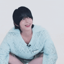 a young man wearing a light blue sweater is smiling while squatting down