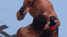a man wearing a pair of ufc gloves is fighting another man on a blue surface .