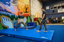 two men are standing on a blue mat in front of a wall that says circus is for everyone