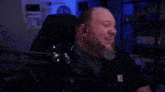 a bald man with a beard is sitting in front of a microphone in a dark room .