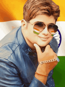 a young man wearing sunglasses and a bracelet is smiling in front of a flag of india