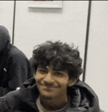a young man with curly hair is smiling in a room .