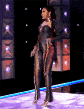a woman in a black and gold jumpsuit is standing on a stage with lights behind her .