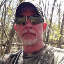 a man with a beard is wearing sunglasses and a hat .
