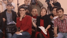 a group of people are sitting in front of a camera and covering their mouths