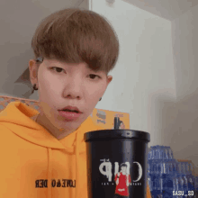 a young man wearing a yellow hoodie is holding a black cup that says cub
