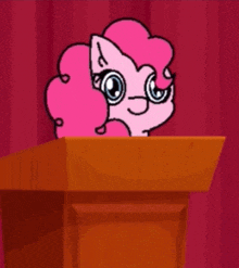 a pink pony is sitting at a podium with a red curtain in the background .
