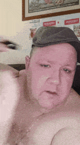 a shirtless man wearing a hat and a necklace is standing in front of a wall with a sign that says become