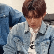 a young man wearing a denim jacket and a white shirt with the letter c on it