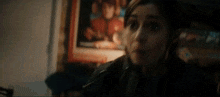 a woman in a black jacket is making a funny face in front of a painting .