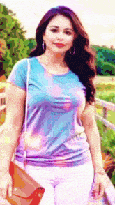a woman in a tie dye shirt and white pants is holding a red purse