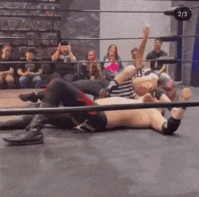 a wrestler is laying on the ground in a wrestling ring while another wrestler holds his hand up .